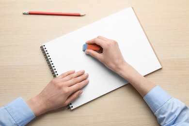 Woman erasing something in notebook at wooden table, closeup