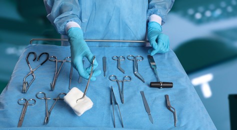 Nurse near table with different surgical instruments in operating room, closeup