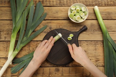 Woman cutting leek at wooden table, top view