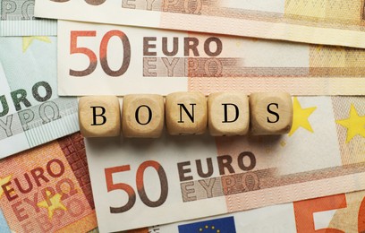 Photo of Wooden cubes with word Bonds on euro banknotes, flat lay