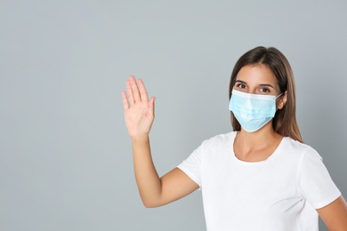 Woman in protective mask showing hello gesture on grey background, space for text. Keeping social distance during coronavirus pandemic