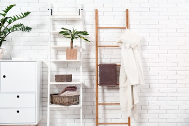 Furniture with clean towels and robe near brick wall in bathroom