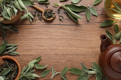 Flat lay composition with cup of sage tea, green leaves and teapot on wooden table. Space for text