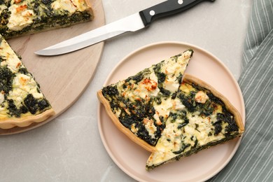 Photo of Pieces of delicious homemade spinach quiche and knife on light table, flat lay