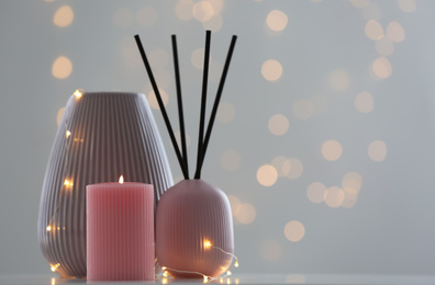 Photo of Vase, burning candle and reed diffuser on table against blurred background with bokeh effect. Space for text