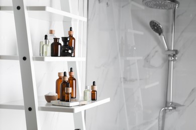 Photo of Essential oils, sea salt, and other cosmetic products on white shelving unit in bathroom. Space for text