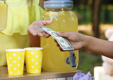 Little girl selling natural lemonade to African-American boy in park, closeup. Summer refreshing drink