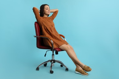 Young woman relaxing in comfortable office chair on turquoise background