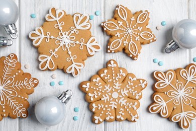 Tasty Christmas cookies and baubles on white wooden table, flat lay
