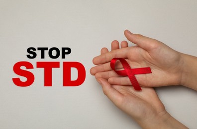 Young woman holding red awareness ribbon on beige background, top view. Stop STD 