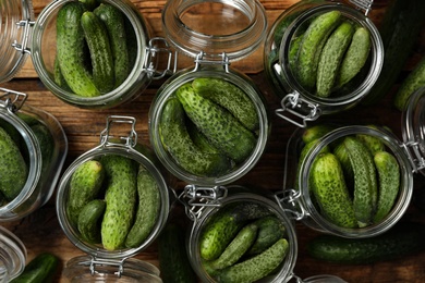 Pickling jars with fresh cucumbers on wooden table, flat lay