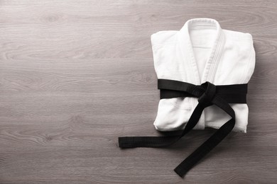 Martial arts uniform with black belt on white wooden background, top view. Space for text