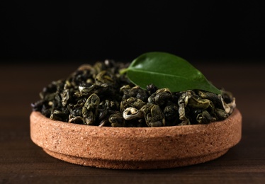Dried green tea leaves in cork bowl on wooden table, closeup