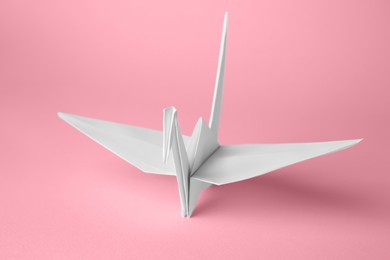 Photo of Origami art. Handmade paper crane on pink background, closeup