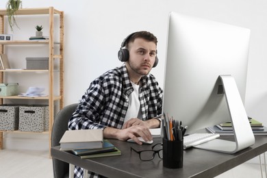 Young man in headphones using modern computer for studying at home. Distance learning