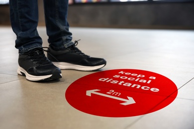 Keep social distance as preventive measure during coronavirus outbreak. Red warning sign on floor in front of man, closeup