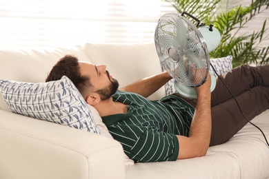 Man with fan lying on sofa home. Summer heat