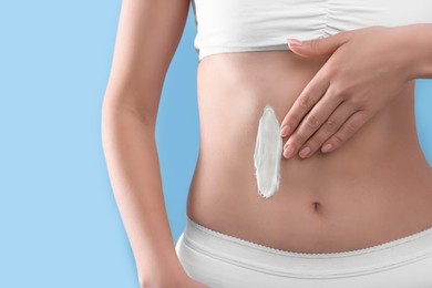 Photo of Woman with smear of body cream on her belly against light blue background, closeup