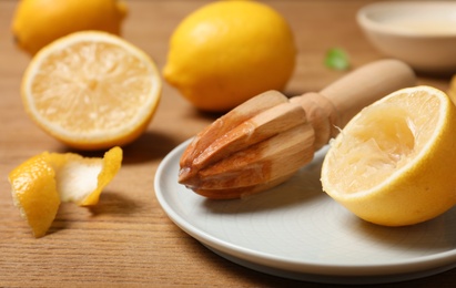 Plate with wooden juicer and lemon half on table. Refreshing drink recipe