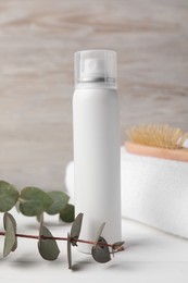 Dry shampoo spray, towel and eucalyptus on white wooden table
