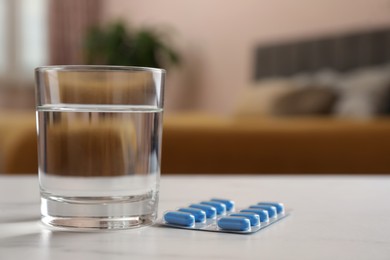 Photo of Glass of water and pills on white table indoors, space for text. Potency problem concept