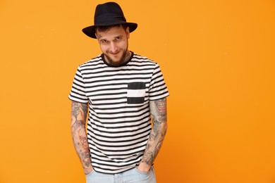 Photo of Portrait of handsome hipster man wearing stylish hat on orange background. Space for text
