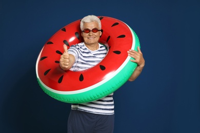 Funny mature man with bright inflatable ring on dark blue background