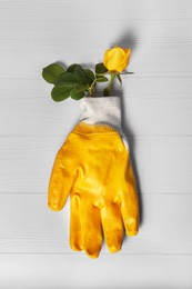 Gardening gloves with beautiful rose on white wooden table, top view