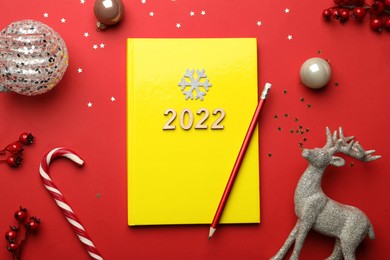 Yellow planner and Christmas decor on red background, flat lay. Planning for 2022 New Year