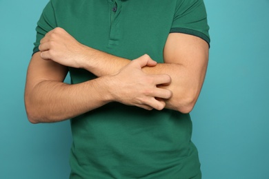 Young man scratching arm on color background, closeup. Annoying itch