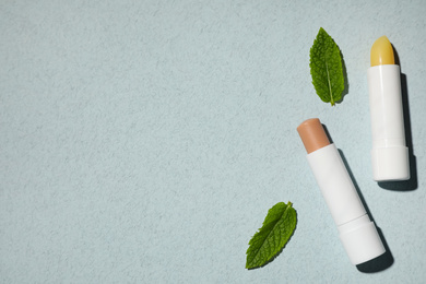 Hygienic lipsticks and mint leaves on light green background, flat lay. Space for text