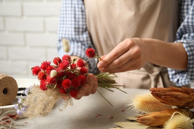 Florist making bouquet of dried flowers at light grey table, closeup