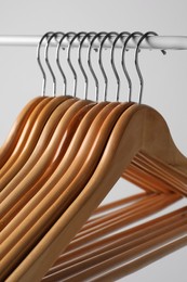 Wooden clothes hangers on metal rail against light grey background, closeup