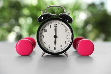 Alarm clock and dumbbells on grey table against blurred background. Morning exercise