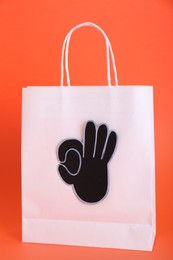 Photo of Paper bag and cutout of okay hand gesture on orange background
