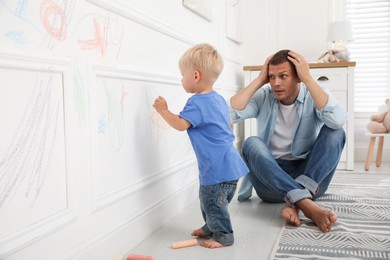 Frustrated father watching his little son drawing on wall at home