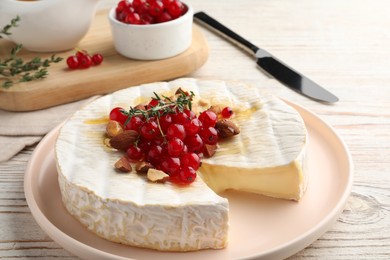 Brie cheese served with almonds, red currants and honey on white wooden table, closeup
