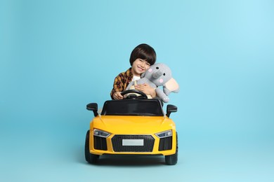 Little child with toy driving car on light blue background
