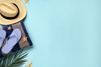 Beach towel, flip flops and hat on light blue background, flat lay. Space for text