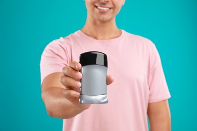 Young man holding deodorant on blue background, closeup. Mockup for design