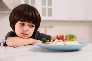 Cute little boy refusing to eat dinner in kitchen
