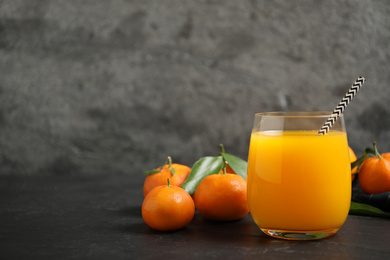 Glass of fresh tangerine juice and fruits on black table. Space for text