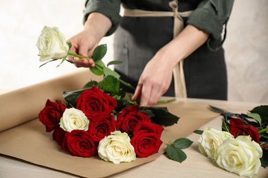 Woman making luxury bouquet of fresh roses at wooden table, closeup