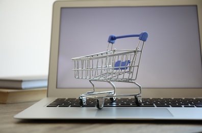 Internet shopping. Laptop with small cart on table, closeup