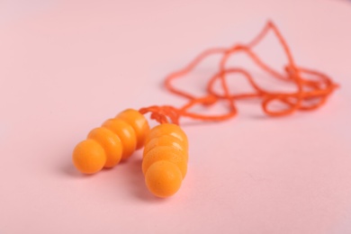 Pair of orange ear plugs with cord on pink background, closeup