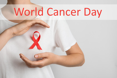 Woman with red ribbon on t-shirt against light background. World Cancer Day