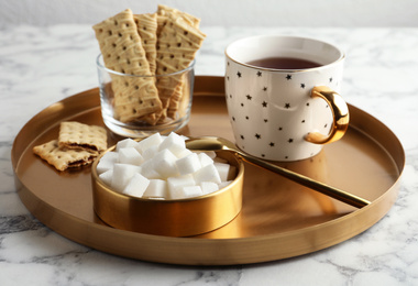 Refined sugar cubes in bowl and aromatic tea on white marble table