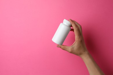 Woman holding bottle of pills on pink background, closeup. Space for text