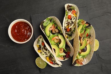 Delicious tacos, lime and sauce on black table, flat lay