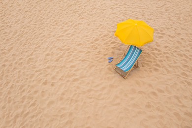 Yellow beach umbrella, sunbed and flip flops on sandy coast. Space for text